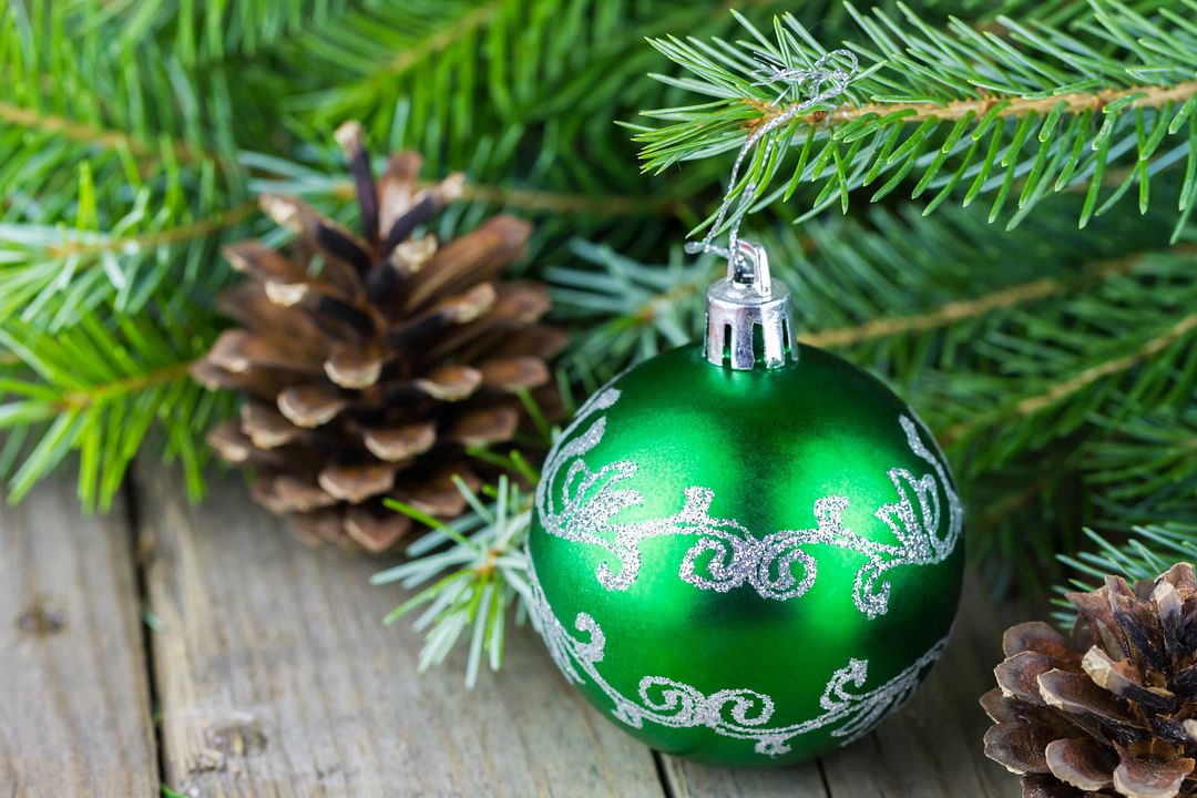 Close-up view of green christmass ball with fur-tree branches and cones on old wooden background