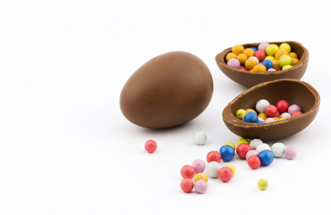 Close-up view of group chocolate eggs full of colorful sweet dragee on white background