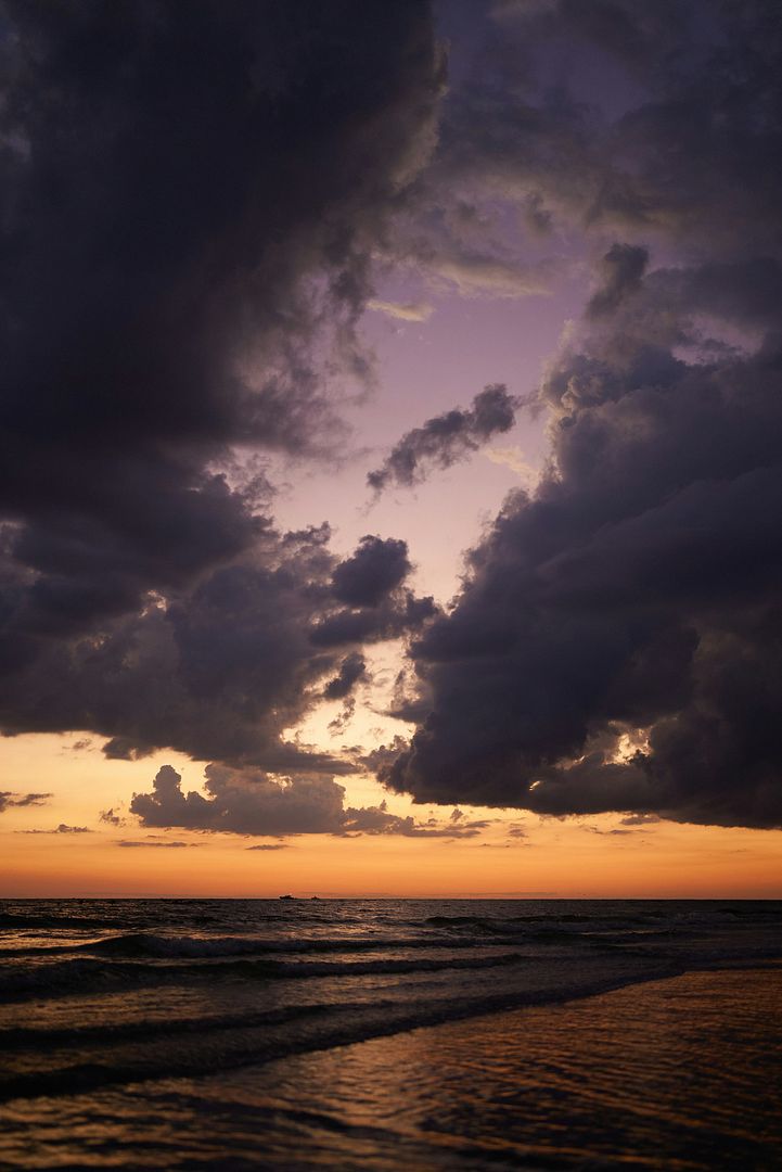 the sun is setting over the ocean on a cloudy day