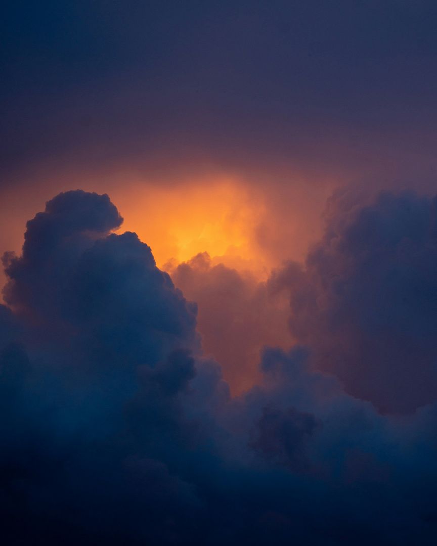 a plane flying through a cloudy sky at sunset