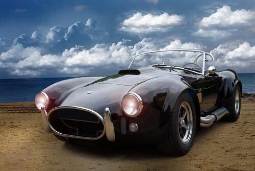 The image shows a classic dark-colored AC Shelby Cobra 427 sports car with an open top.  The AC Shelby Cobra 427 is a two—seat British-American sports roadster.   History of creation: in the late 1950s, American racing driver and engineer Carroll Shelby conceived an ambitious project - the fastest car in the world. He enlisted the support of the Ford Corporation and installed a powerful American V8 in the lightweight body of the British AC Ace roadster.   1962 specification: equipped with a 4.3-liter V8 with 260 horsepower and accelerated to "hundreds" in 5.5 seconds, reaching a maximum speed above 230 km/h.   Third generation (Mk III): under the hood was a 7-liter V8 Ford 427, built for NASCAR racing. It was one of the most powerful engines of the 1960s, developing 485 horsepower in a racing configuration, and also quite impressive 410-425 hp in a civilian configuration..   Body: despite its external similarity to the AC Ace, it was seriously modified to meet increased loads and became more "muscular". This Cobra accelerated to 100 km/h in 4.7 seconds.   Top modification 427 S/C (Semi/Competition): the engine produced 485 forces and, in fact, it was a racing car available to everyone. Only citizens with serious training could handle the car.   Production: from 1962 to 1967. 998 copies of this model were produced, of which 343 pieces are the most recognizable and legendary 427 variety.