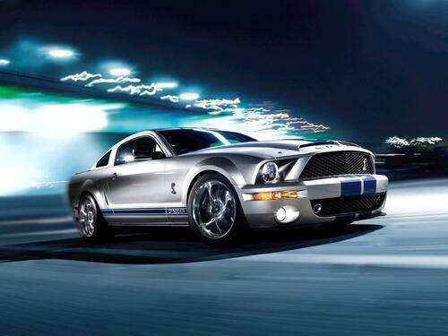 The image shows a silver Ford Mustang Shelby GT500 sports car with dynamic lighting.  The Ford Mustang Shelby GT500 is a high—performance modification of the legendary Ford Mustang belonging to the GT series.   The first GT500 presentation took place in 1967. The main feature of the new modification was the 7-liter Ford Cobra V8 engine. The powertrain was reinforced with 2 four—chamber Holley Performance carburettors, which increased its power to 400 hp (officially 355 hp).